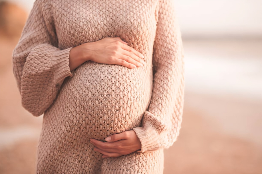 Expectant mom in a cozy beige dress, gently holding her belly with both hands