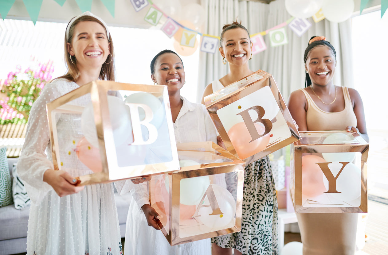 Four smiling women at a baby shower, holding cubes with the word 'baby'.