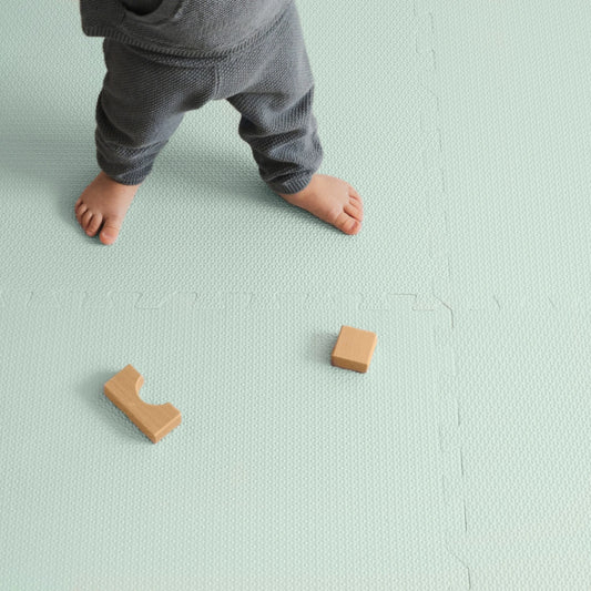 Toddler standing on a cushioned, soft foam mat in turquoise grey