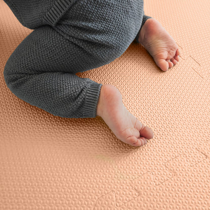 Baby crawling on an EVA foam puzzle play mat in summer peach