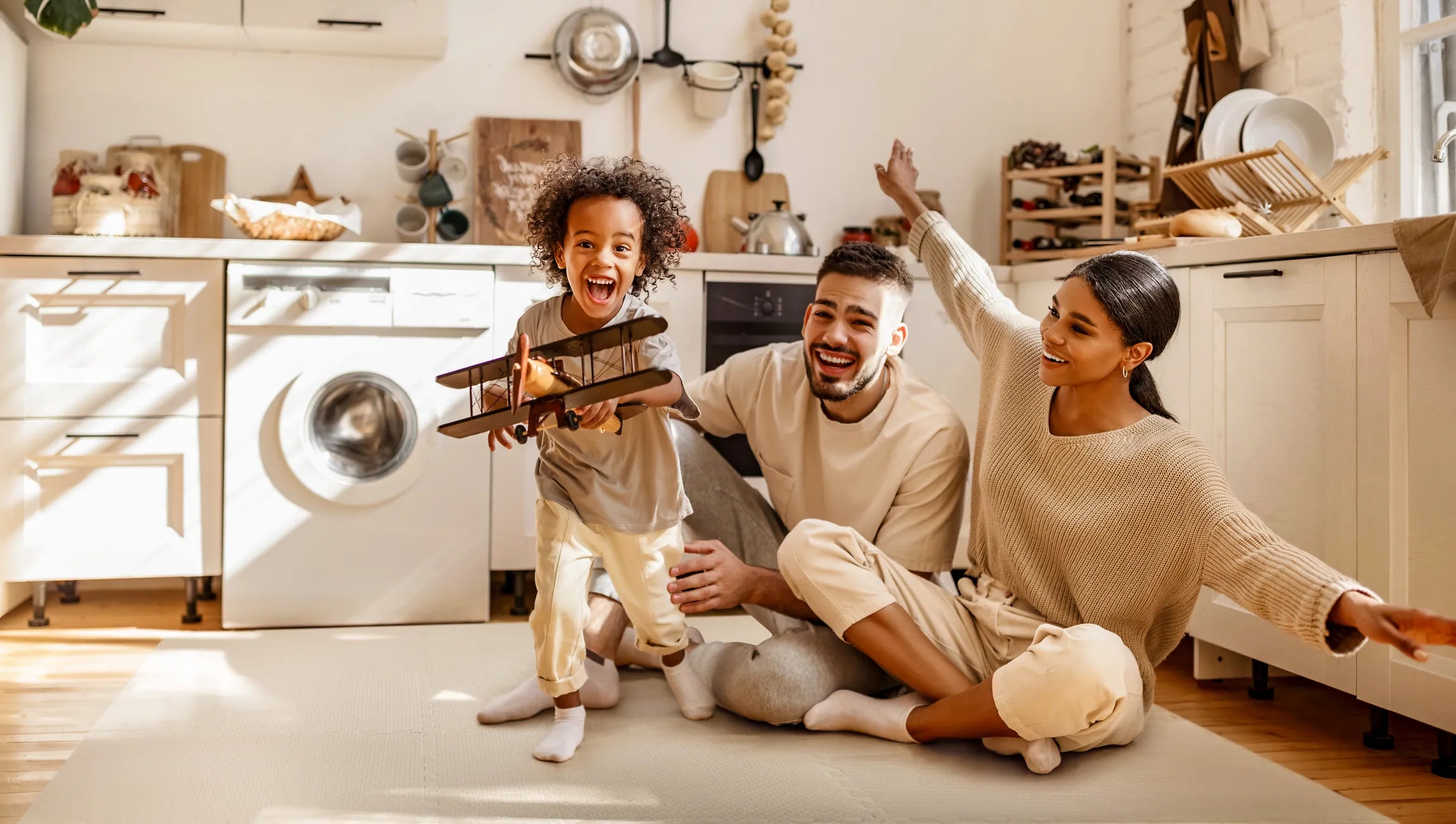 Family playing with a toddler on premium baby play mats in siesta sand in a bright modern kitchen